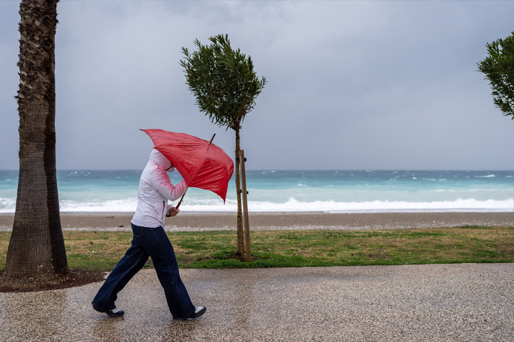 Sommer, Sonne Planänderung Symbolfoto: Frau mit Regenschirm im Sturm am Meer